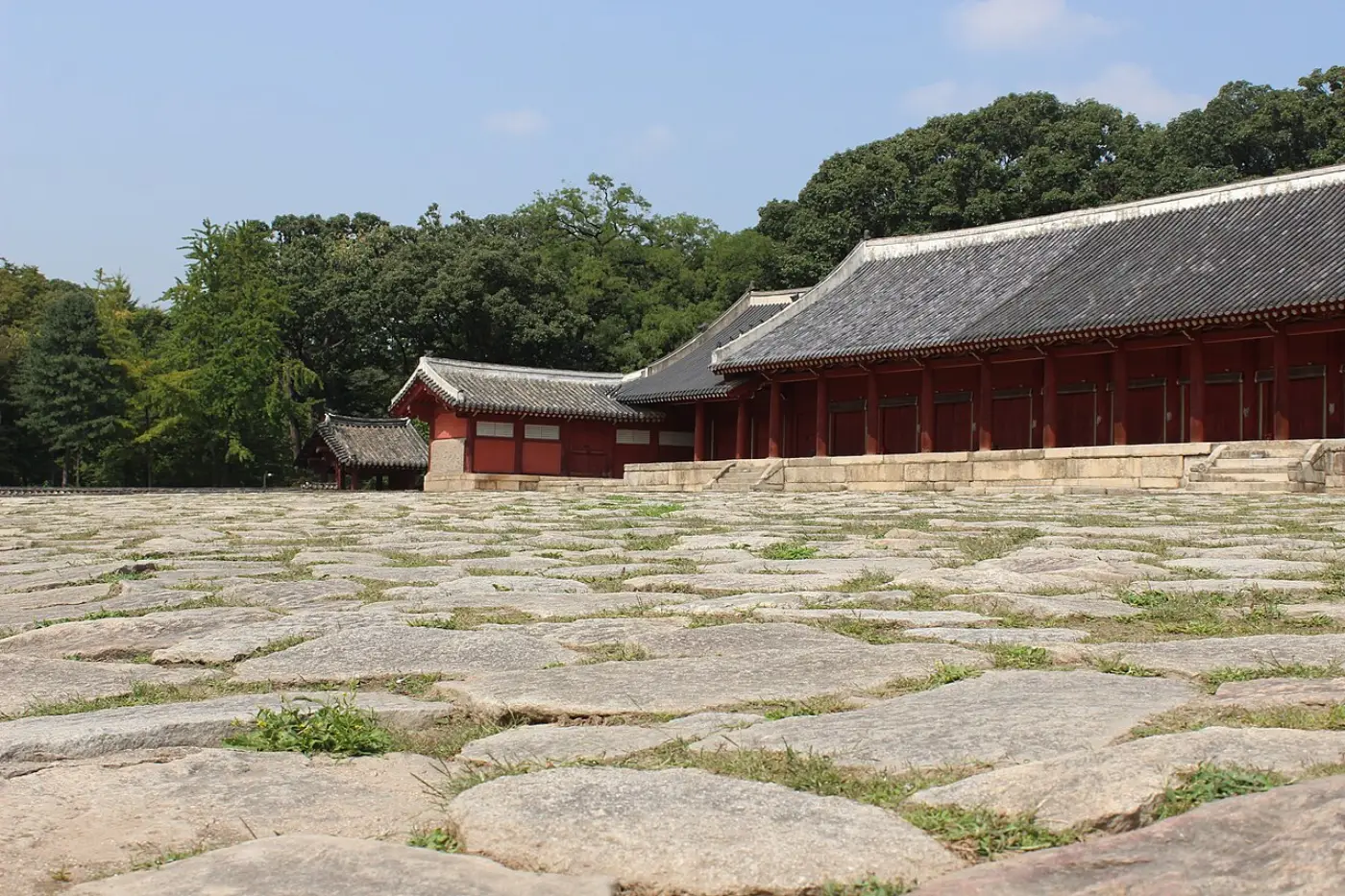Long Jongmyo hall with red columns behind a wide stone-paved terrace